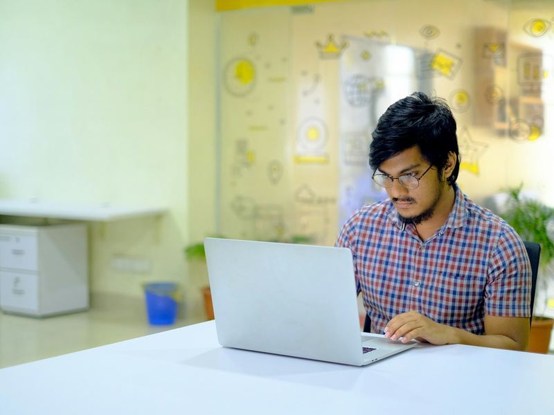 A young man working on a laptop at a desk in an office