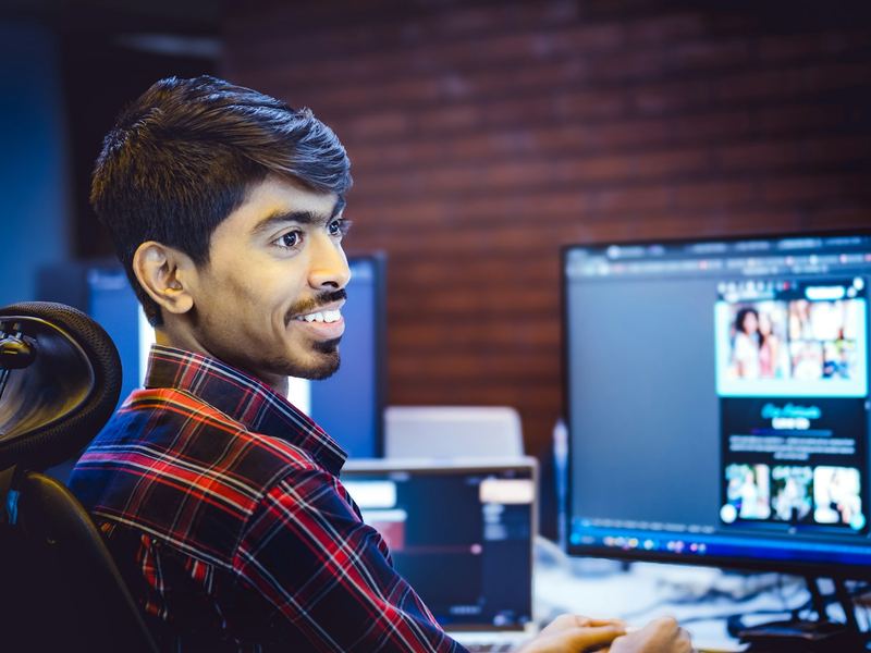A smiling young developer working at a computer with two monitors