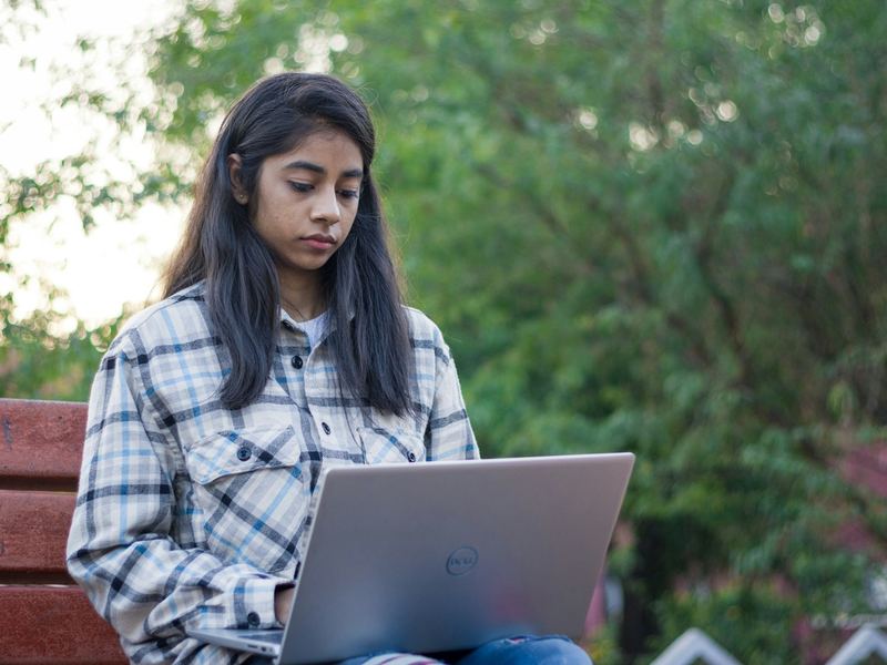 A student using a laptop on a bench outdoors