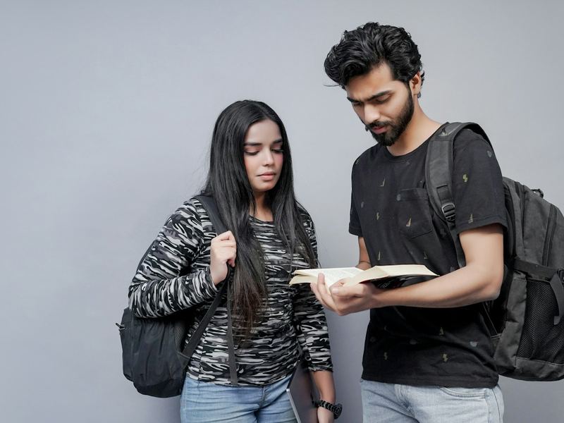 Two students with backpacks looking at a notebook