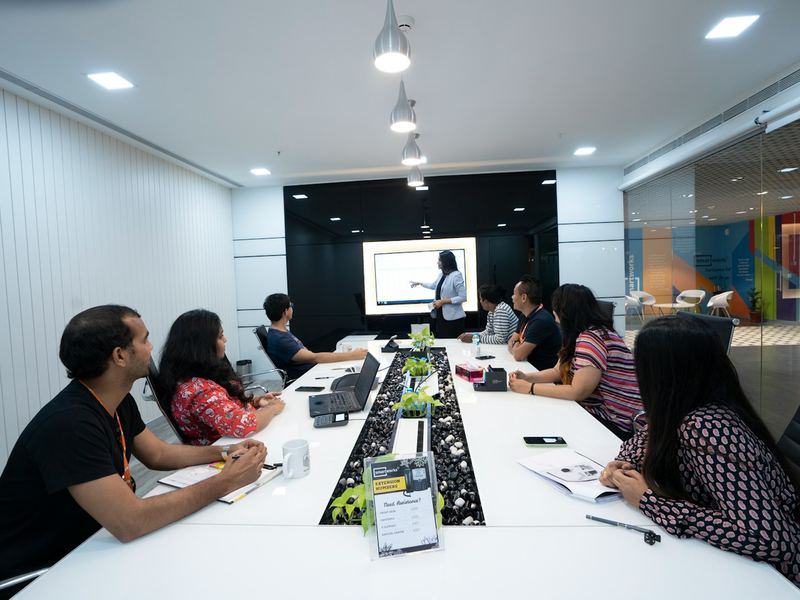 Trainees with laptops at a long table in a modern training room